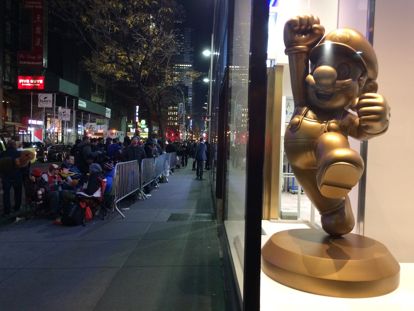 A lineup in front of the Nintendo NYC Store, with a golden-coloured Mario statue in the shop's window.