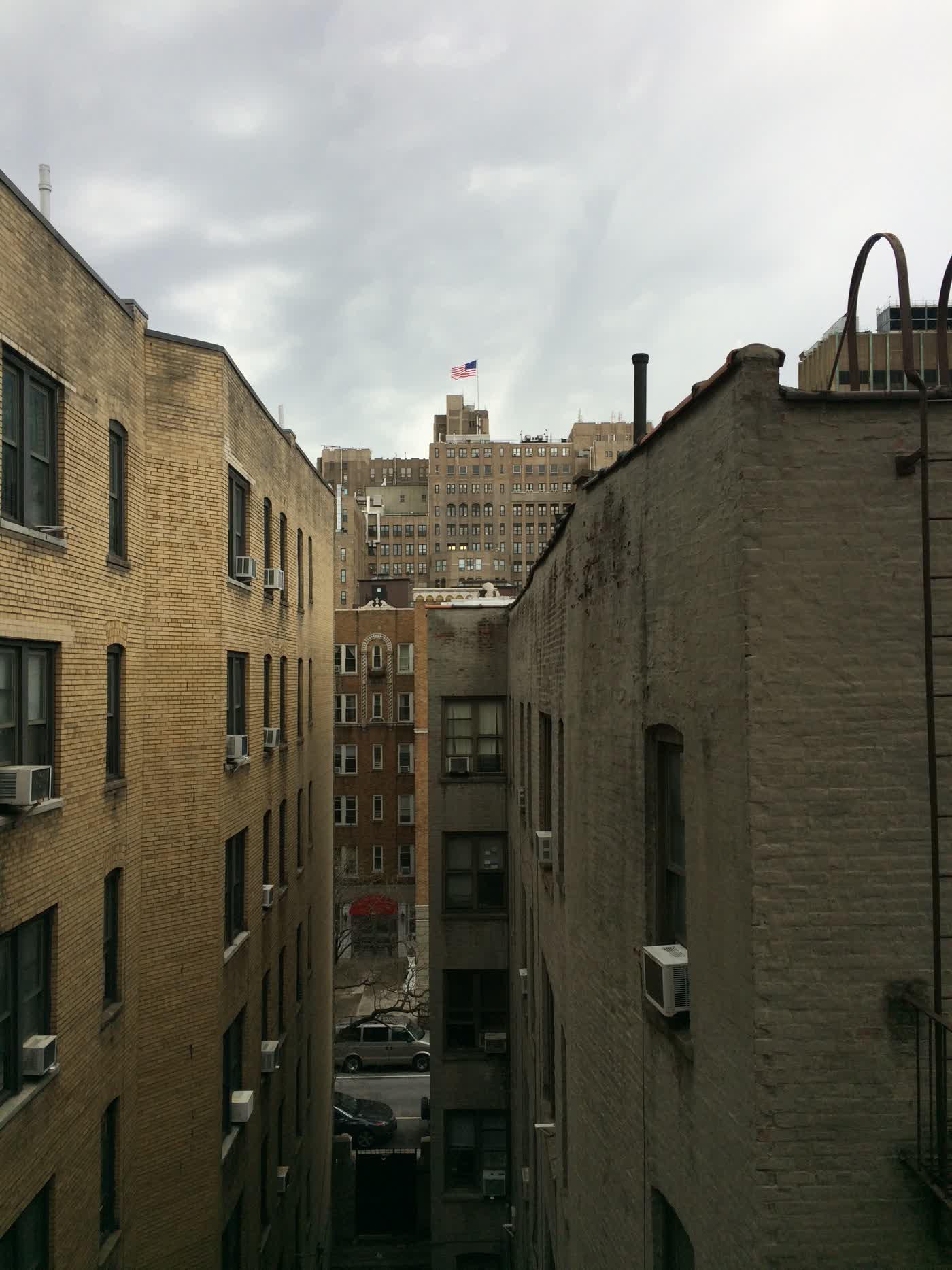 A corridor between buildings, culminating in a larger building with an American flag on top.