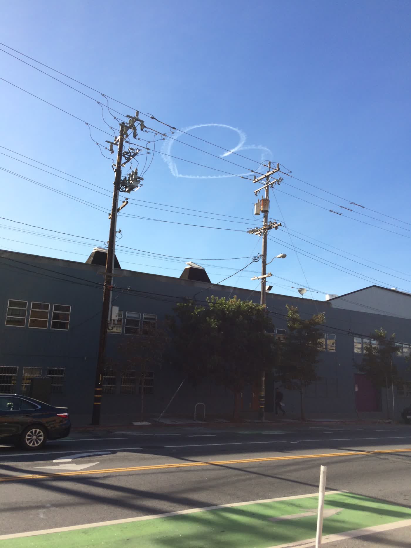 An airplane contrail drawn in the shape of a heart above a Bay Area street.