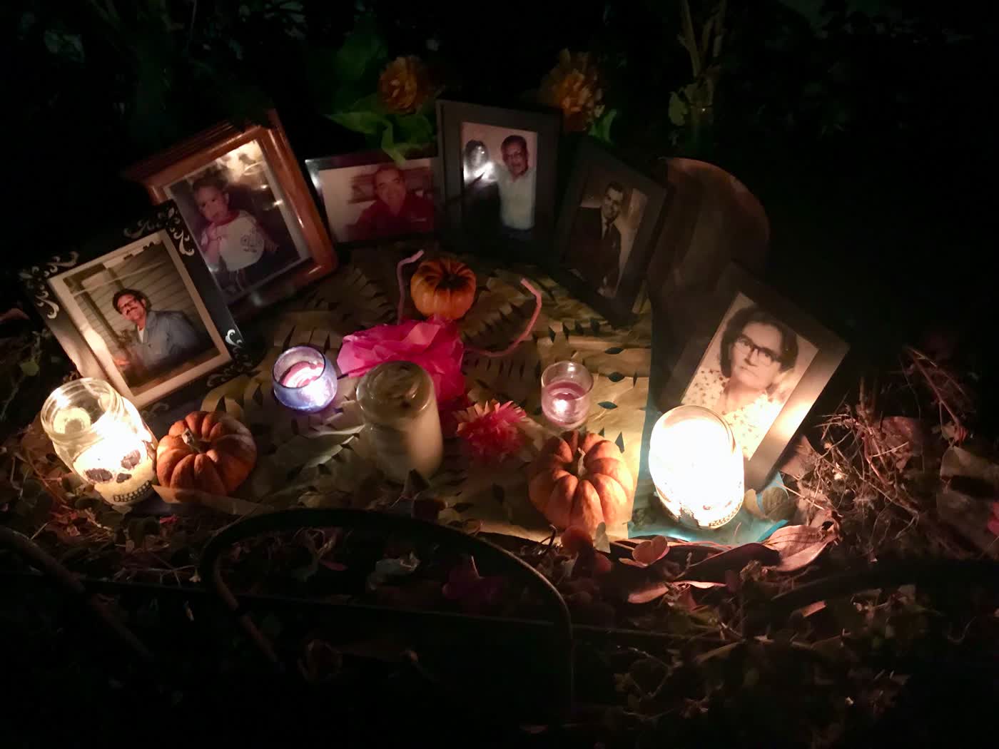 An ofrenda, with several framed pictures of people amidst candles and tiny pumpkins.