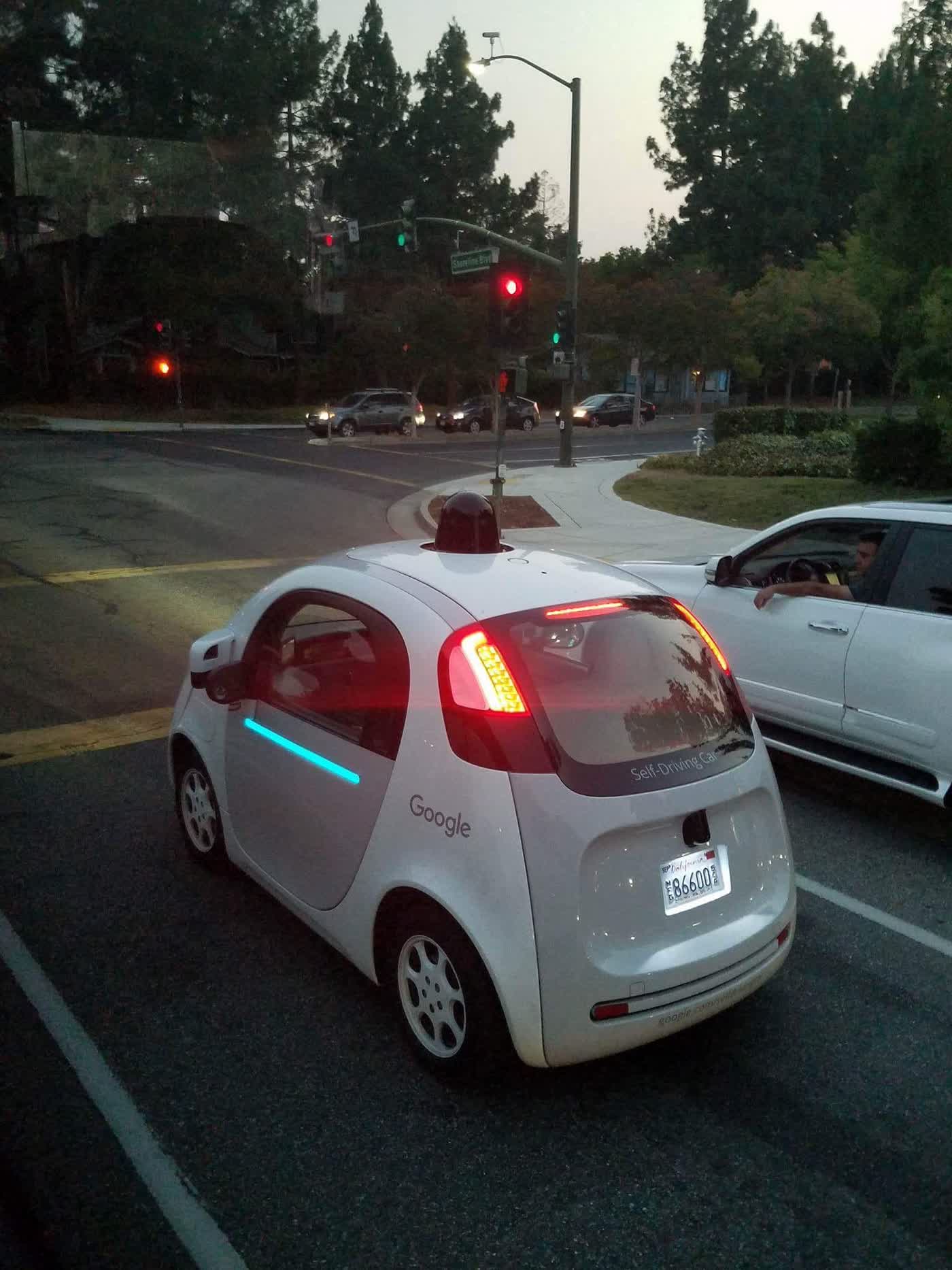 A Google self-driving car waiting at a stoplight. The car is short, appearing to be a two-seater, with an unusual dome shape.