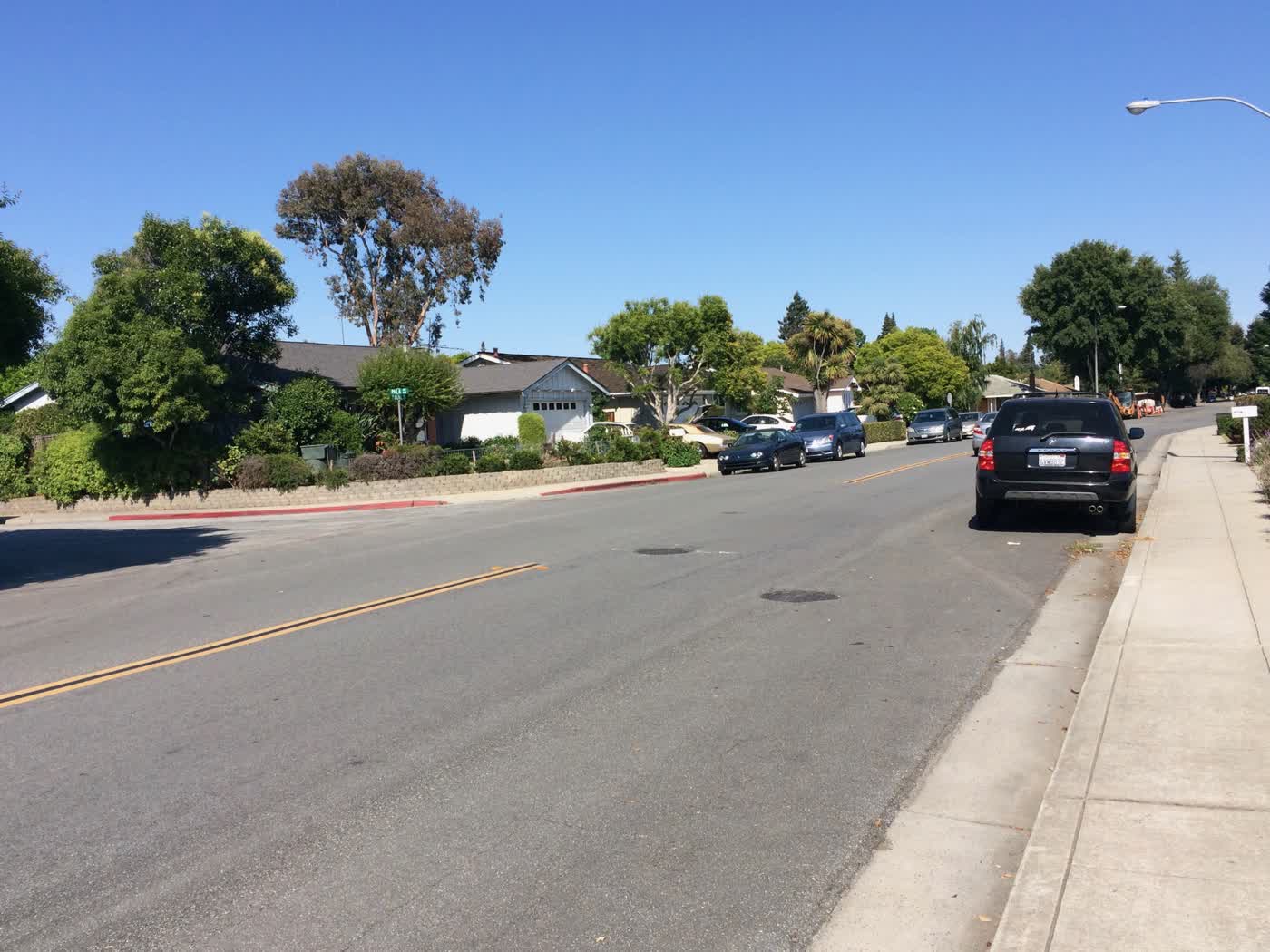 A suburban road with some single-story single-family homes and parked cars.