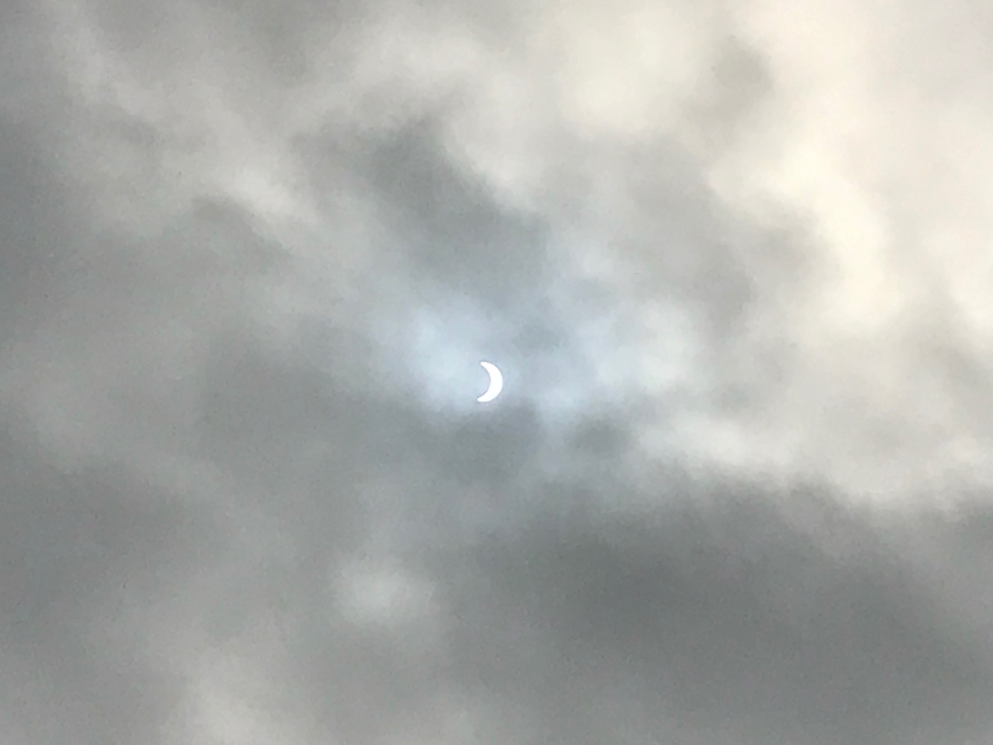 The sun at the peak of the partial eclipse of 2017, as seen through some clouds. Most of the sun is obscured by the moon, leaving a crescent shape.