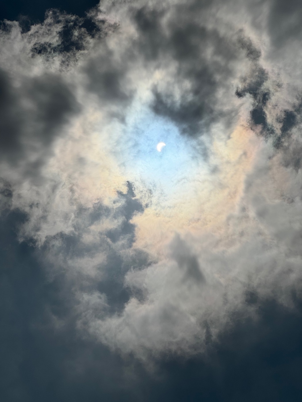 The sun during the initial stages of partiality in 2024, partly hidden behind some iridescent clouds.