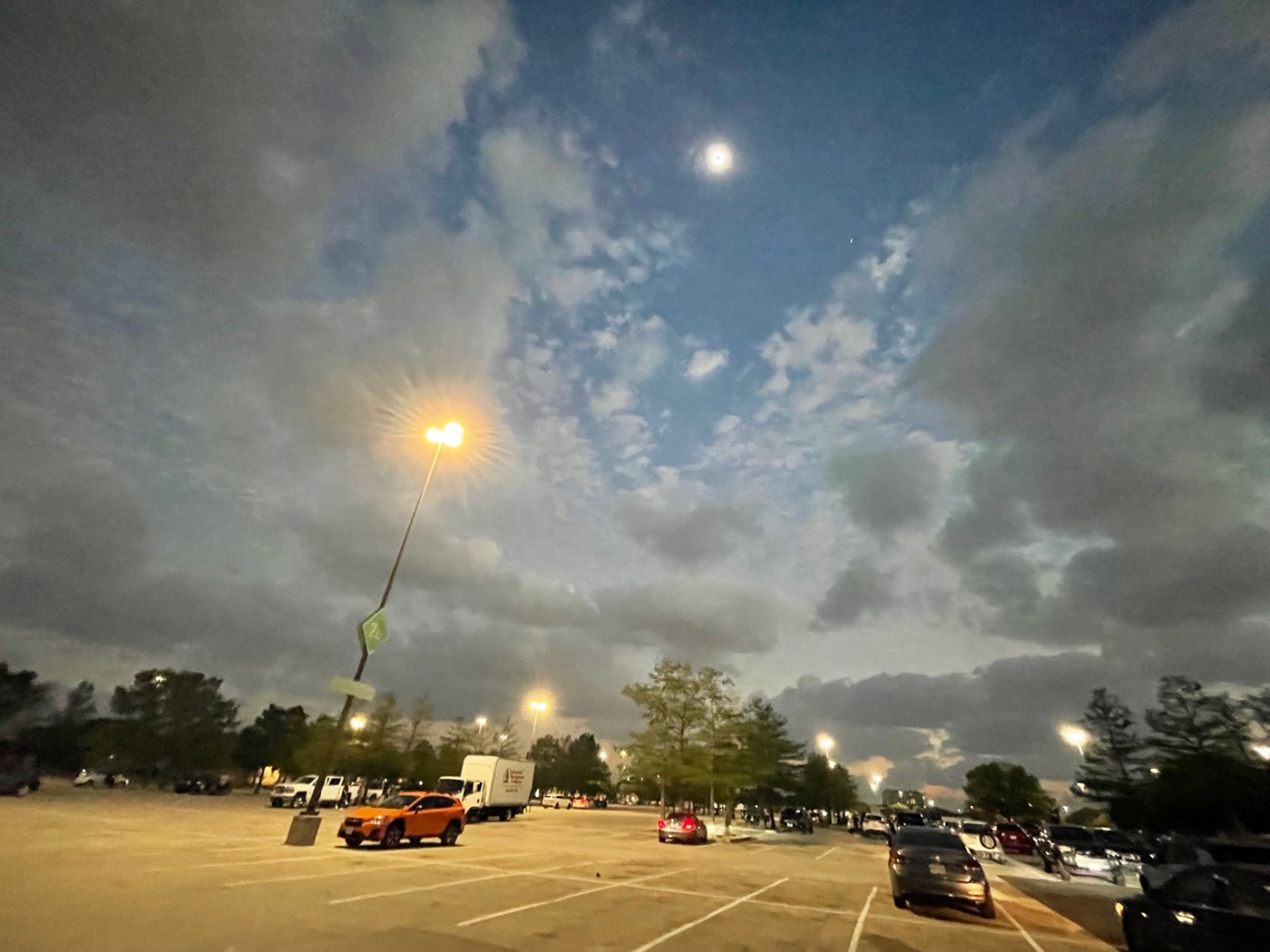 The parking lot we were in, the eclipsed sun visible towards the top of the image, a streetlight visible to the left. One small star is visible at the bottom-right of the sun.